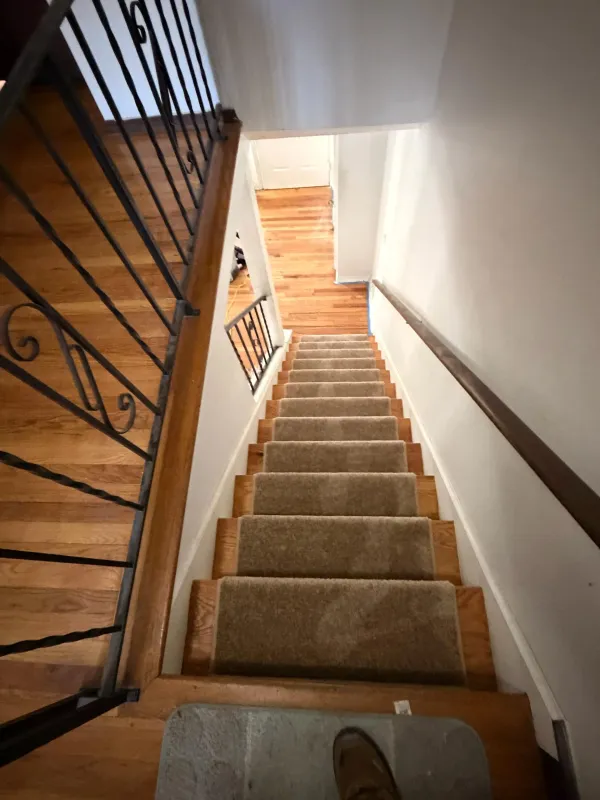 Interior view of a wooden staircase with carpet runners and wrought iron railings